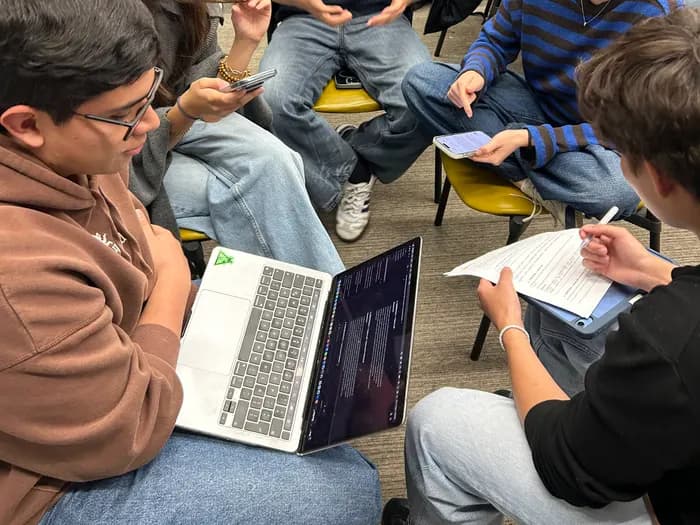 Célula de estudiantes construyendo un prototipo con portátil y notas